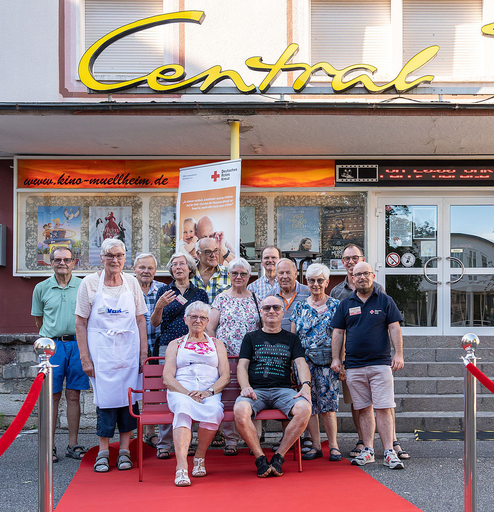 Rote bank-Kino&Wein Auf dem Bild sind mehrere Personen auf einer roten Bank zu sehen.