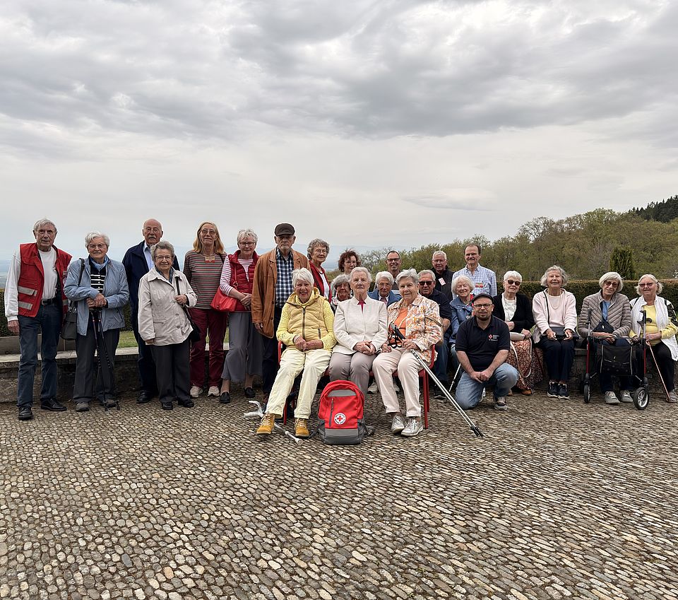 Rote Bank der Begegnung-Seniorenausflug Auf dem Bild sind ist eine große Gruppe mit einer roten Bank zu sehen.