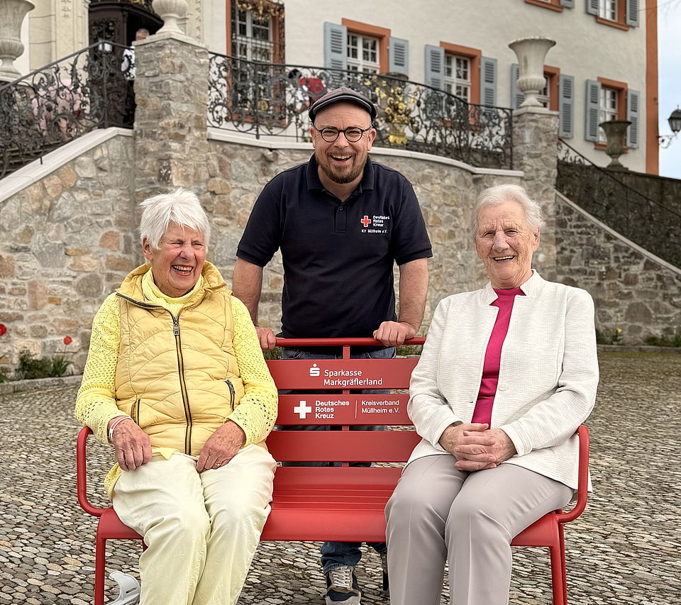 Rote Bank der Begegnung Auf dem Bild sind 3 Rotkreuzler mit der Bank der Begegnung zu sehen.