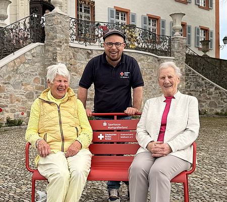 Auf dem Bild sind 3 Rotkreuzler mit der Bank der Begegnung zu sehen.