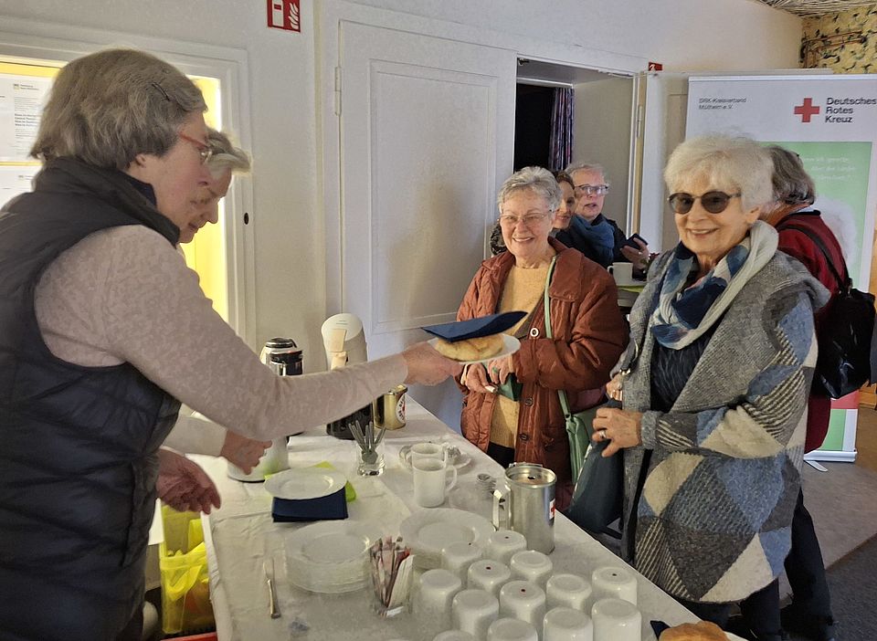 Auf dem Bild sind ehrenamtliche Rotkreuzlerinnen zu sehen, die Kaffee und Corissants ausgeben.
