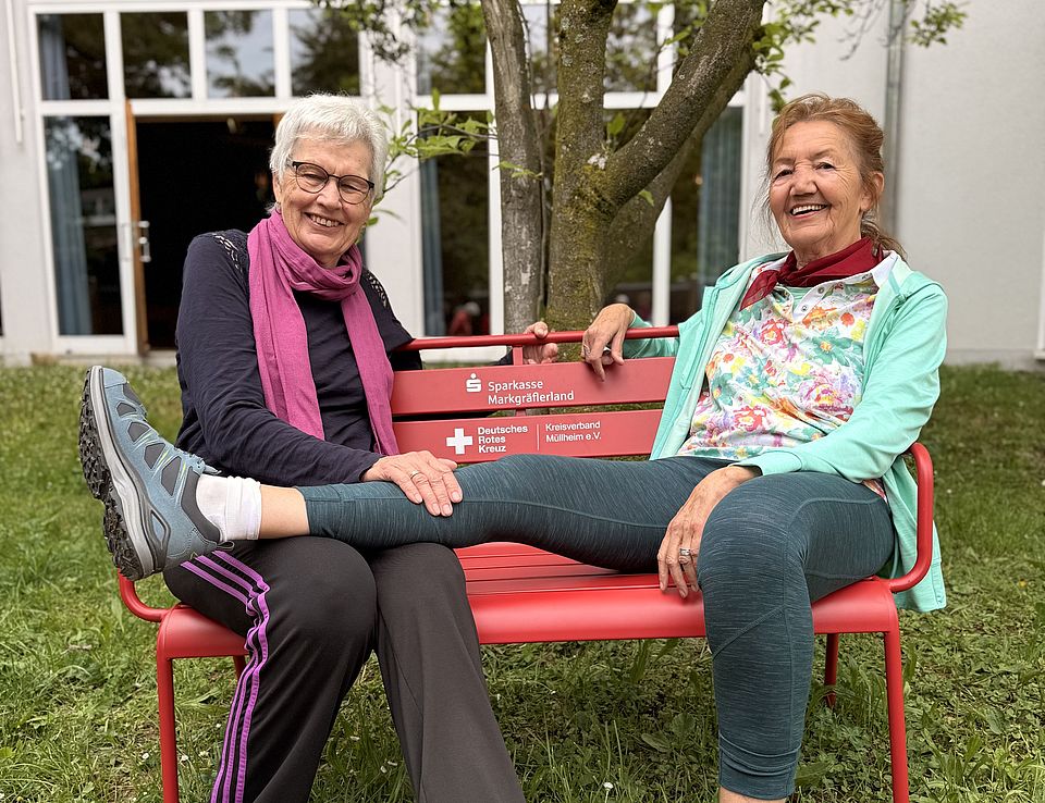 Rote Bank der Begegnung-Seniorengymnastik Auf dem Bild sitzen 2Senioreinnen auf einer Roten Bank.