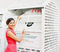 Kleidersammlung des DRK und Altkleidercontainer: junge Frau wirft einen Sack mit Altkleidern in einen Container des DRK