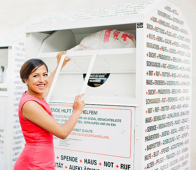 Kleidersammlung des DRK und Altkleidercontainer: junge Frau wirft einen Sack mit Altkleidern in einen Container des DRK